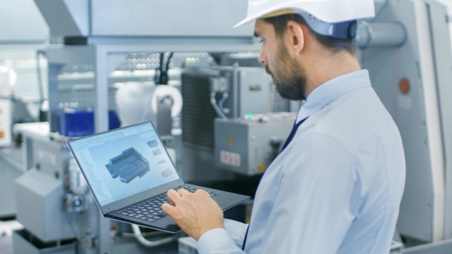 Chief Engineer in the Hard Hat Holds Laptop with 3D Component Model on it's Screen. In the Background Modern Factory Equipment.#asset:6070@1:alt