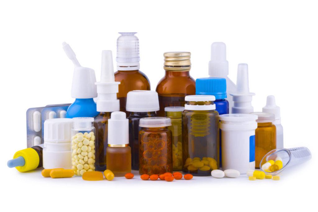 Assorted pharmaceutical containers: amber glass bottles, nasal sprays, pill jars, a blister pack and loose tablets